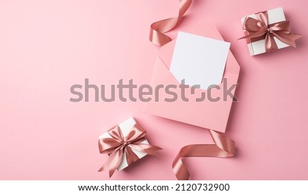 Top view photo of valentine's day decor two white gift boxes with pink bows curly silk ribbon and open pink envelope with paper sheet on isolated pastel pink background with blank space