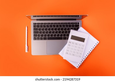 Top View Photo Of White Calculator Pen And Notebook On Grey Laptop On Isolated Orange Background
