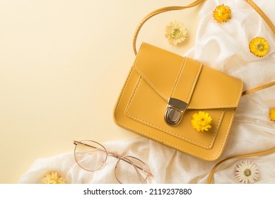 Top view photo of woman's day composition yellow leather purse stylish spectacles white textile and wild flowers on isolated beige background with blank space