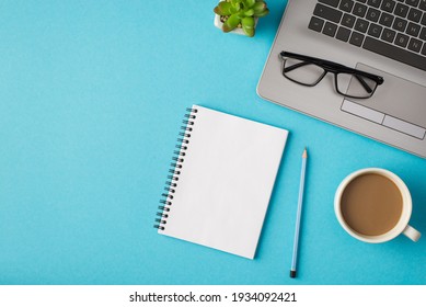 Top view photo of workplace with glasses on laptop pencil notebook plant and cup of coffee on isolated blue background with copyspace