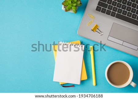 Top view photo of workplace with laptop yellow chancellery notebooks plant and cup of coffee on isolated blue background with blank space