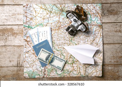 Top View Photo Of World Map, White Paper Plane, Passport, Tickets, Money And Vintage Camera. Objects Are On Light Colored Wooden Floor