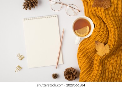 Top view photo of yellow knitted sweater cup of tea with lemon yellow autumn leaves golden binder clips pencil pine cones stylish glasses and planner on isolated white background with blank space