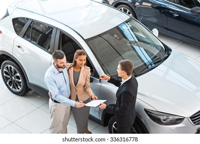 Top view photo of young male consultant and buyers signing contract for new car in auto show. Concept for car rental