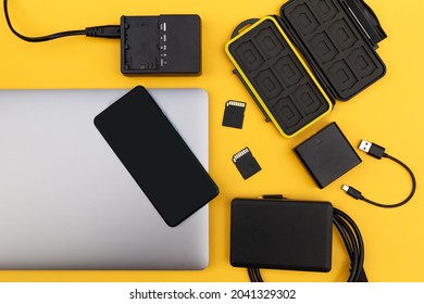 Top View Of A Photographer's Desk Showing A Laptop Computer, Mobile Phone, Card Holder, Memory Cards, Hard Disk, Camera Battery And Charger.