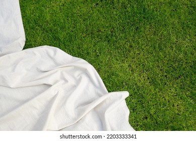 top view of picnic blanket on ground, advertising concepts, copy space. linen tablecloth or white textile plaid on green lawn in garden outdoor at summer day, flat lay - Shutterstock ID 2203333341
