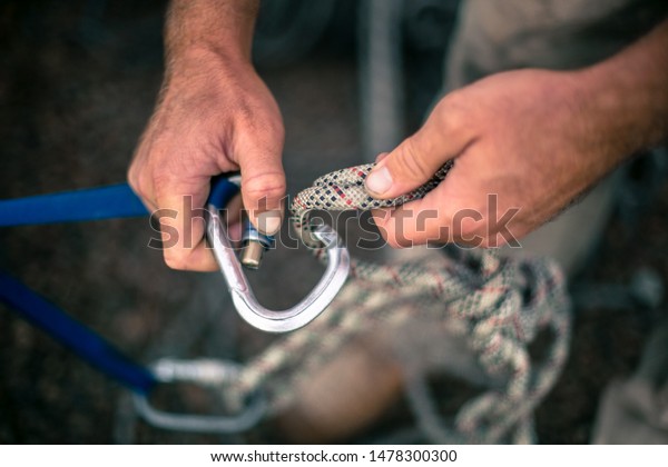 Top view picture of industrial rope access worker\
hand connecting locking screwgate Karabiner 2.5 tone Nylon low\
stretch rope which its attached onto safety tape sling and beam\
structure anchor point