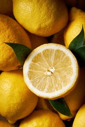 Top View Picture Of Many Lemons Filling The Shot. High Contrast Vibrant Yellow Color. Beautiful Texture Of The Citrus. One Lemon Is Sliced And Has Leaves Around It.