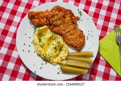 Top view picture on the deep fried chicken escalope or schnitzel with mashed potatoes and pickled cucumbers. Served on white plate with green spring napkin and cutlery. Traditional czech cuisine.