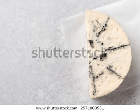Top view of piece (wedge, slice) of blue cheese, gorgonzola, roquefort of creamy texture, naturally aged. Delicious Italian or French traditional cheese variety. Close up view, copy space. Grey table