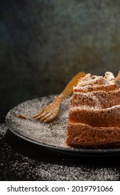 Top View Of Piece Of Yogurt Sponge Cake On Dark Plate With Sugar And Wooden Fork, Selective Focus, On Wooden Table And Gray Background, Vertical