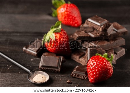 Top view of pieces of chocolate bar with strawberries on wooden table, horizontal, with copy space