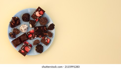 Top View Of Pieces Of Different Chocolates On Blue Plate, Handmade Craft Chocolate And Praline Broken Into Pieces, Copy Space, Template Or Confectionery Banner