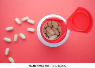 top view of pills spilling from a container on red 