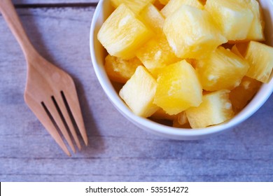 Top View Of Pineapple Chunks In A Bowl On A Wooden Table.