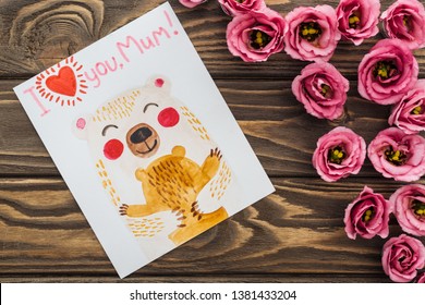 Top View Of Pink Eustoma Flowers And Card With I Love You Mum Lettering On Wooden Table