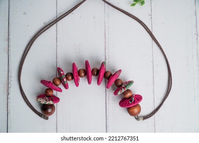 Top View Pink Fabric Necklace With Coconut Shell Beads On White Wooden Table. Etnic Handmade Jewelery.