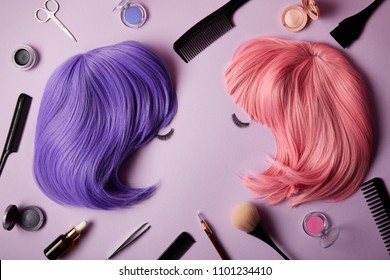 vue de dessus de perruques roses et violettes, faux cils, outils de maquillage et cosmétiques sur le violet