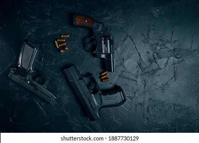 Top view of pistols and copper bullets on black concrete table. Vintage revolver with a drum. 9mm handgun. Criminal or police arsenal. Several types of dangerous firearms. Flat lay and copy space.