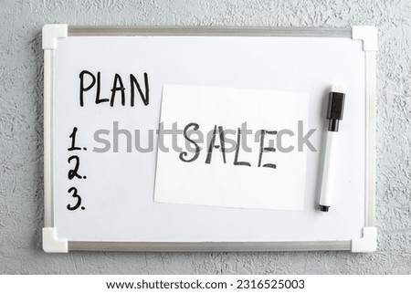 Top view of PLAN and numbers on white desk SALE writing marker on white sheet on gray sand background