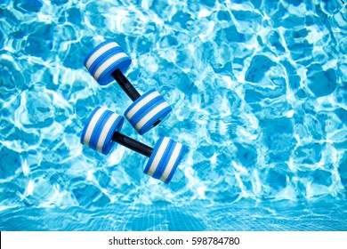 Top view of  plastic dumbbells for aqua aerobics  floating in blue water of swimming pool on summer day outdoors