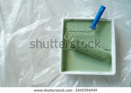Top view of plastic tray with paintroller and green paint standing on the floor covered with cellophane and prepared for renovation work