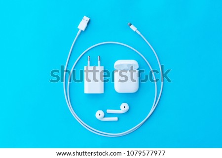Top view plastic white wireless headphones for smartphone, charging case, Lighning USB, adapter on a pastel blue background. Copy space.