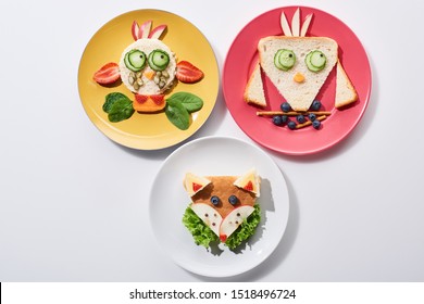 Top View Of Plates With Fancy Cow, Bird And Fox Made Of Food For Childrens Breakfast On White Background