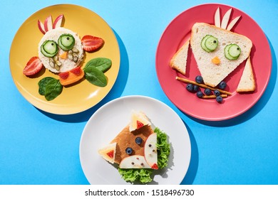 Top View Of Plates With Fancy Cow, Fox And Bird Made Of Food For Childrens Breakfast On Blue Background