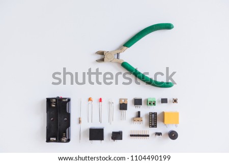 Top view of pliers and electronics component such as resistor, ICs, capacitor, switch, and connector on white background.