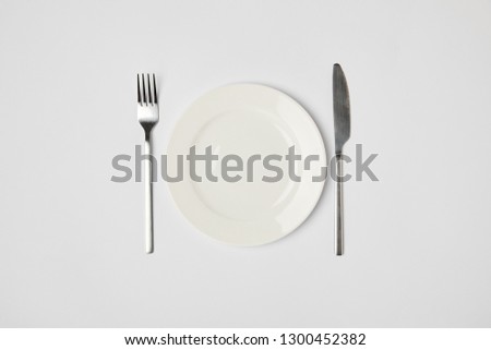 top view of porcelain plate with fork and knive on grey background