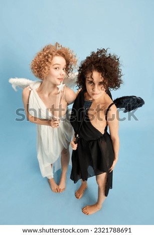 Top view portrait of beautiful young women in image of cute angel and confident demon over blue background. Concept of love, faith, cheating, temptation and innocence, comparison of being, creativity