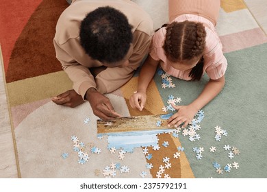 Top view portrait of Black father and daughter playing with jigsaw puzzle together while lying on colorful soft carpet, copy space - Powered by Shutterstock