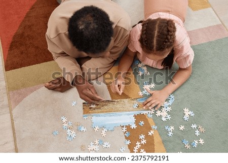 Top view portrait of Black father and daughter playing with jigsaw puzzle together while lying on colorful soft carpet, copy space