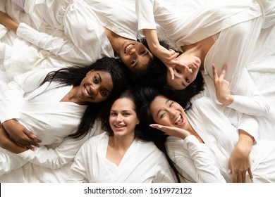 Top View Portrait Of Happy Multiracial Millennial Girls In Bathrobes Lying On Bed Smiling Posing At Bridal Shower, Overjoyed Diverse Female Friends Have Fun Celebrate Bachelorette Hen Party At Home