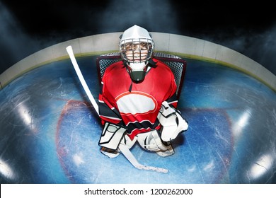 Top View Portrait Of Young Goaltender, Boy In Protective Equipment, Standing With Hockey Stick In The Goal Crease At The Rink