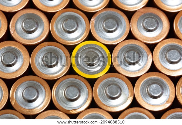 Top view of positive poles of 1.5 V AA Alkaline\
batteries. Battery with yellow outer layer coating in the middle in\
selective focus. Close-up non-rechargeable used batteries.\
Differences concept.