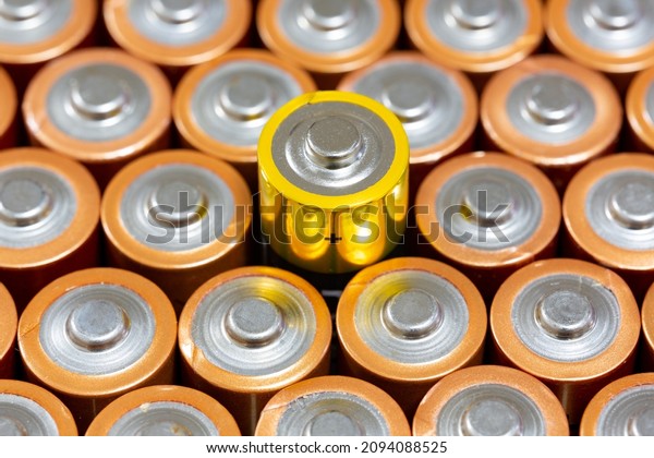 Top view of\
positive poles of 1.5 V AA Alkaline batteries. Battery with yellow\
outer layer coating in selective focus. Above the yellow plated\
battery values. Differences\
concept.