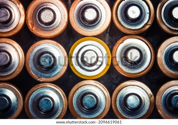 Top view of positive poles of 1.5 V AA Alkaline\
batteries. Battery with yellow outer layer coating in the middle in\
selective focus. Close-up batteries. Differences concept with\
vintage color tones.
