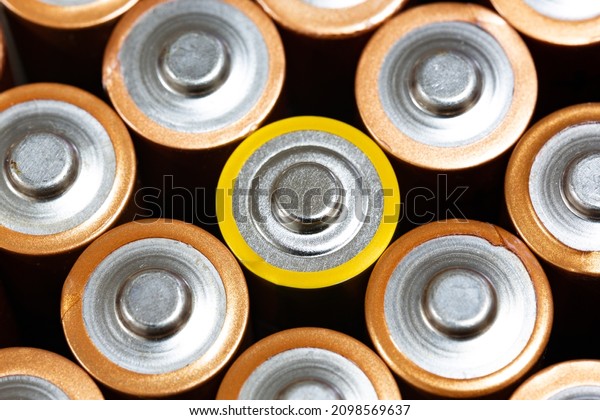 Top view of positive poles of 1.5 V AA Alkaline\
batteries. Battery with yellow outer layer coating in the middle in\
selective focus. Close-up non-rechargeable batteries. Differences\
concept.