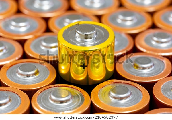 Top view of positive poles of 1.5 V AA Alkaline\
batteries. Battery with yellow outer layer coating in selective\
focus. Differences concept.