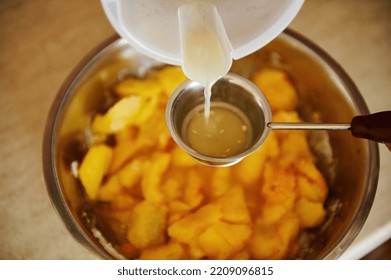 Top View Of Pouring Lemon Juice Into A Metal Bowl With Sliced Peaches While Preparing Homemade Peach Confiture. Canning Peach. Preparing Delicious Jam