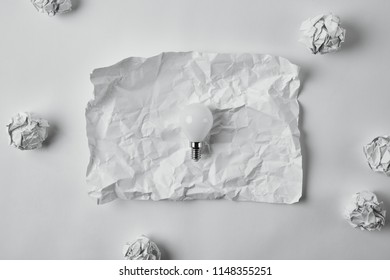 top view of power saving light bulb on crumpled blank paper on white surface