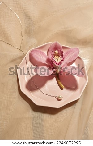 Top view of precious chainlet and pink flower on plate on silk cloth background. Stylish glamour elegant and luxury jewelry. Studio shoot. Nobody. E-commerce. Copy space