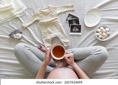 Top view of pregnant woman in the bed preparing baby clothes at home, pregnancy and birth concept