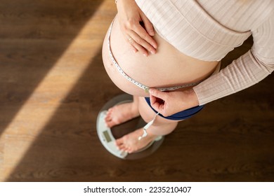 Top view of pregnant woman measuring her belly and checking her weights at home - Powered by Shutterstock