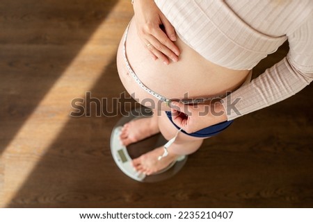 Top view of pregnant woman measuring her belly and checking her weights at home