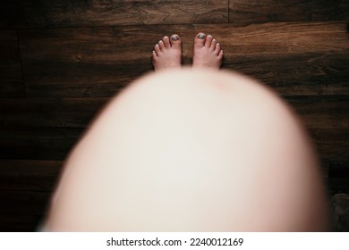 A top view of a pregnant woman's belly standing shoeless on the floor - Shutterstock ID 2240012169