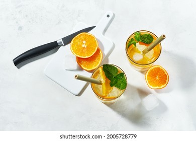 Top view of prepering summer cockteil. Glasses with gin and cold tonic with orange and mint, decorated with slices and with ice cubes on white background and bamboo straw.
