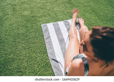 Top view of pretty female`s feet sunbathing on the stripped towel lying on green grass near swimming pool. Safe skin protected tanning concept image.